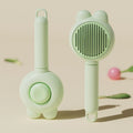 Self-cleaning pet brush with green handle and stainless steel teeth, showing release button mechanism