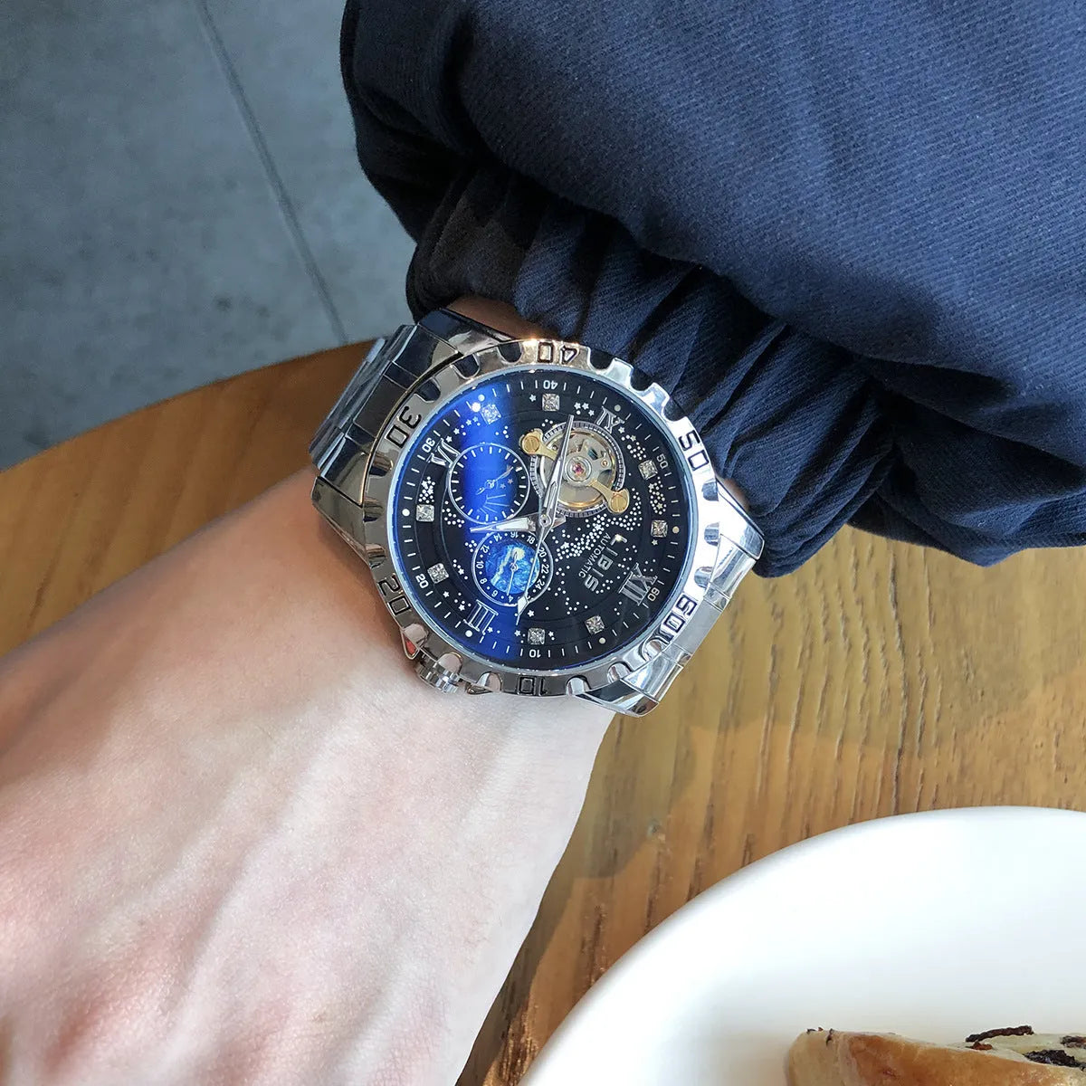 Men's silver case automatic watch with black steel strap and luminous dial.