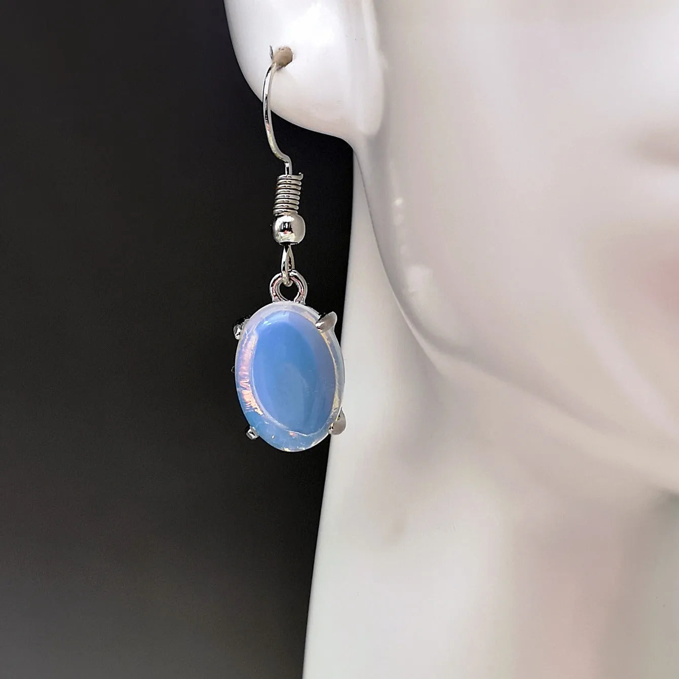 A pair of opal-coloured dangle earrings with a cross pendant, in a drop shape on a white background.