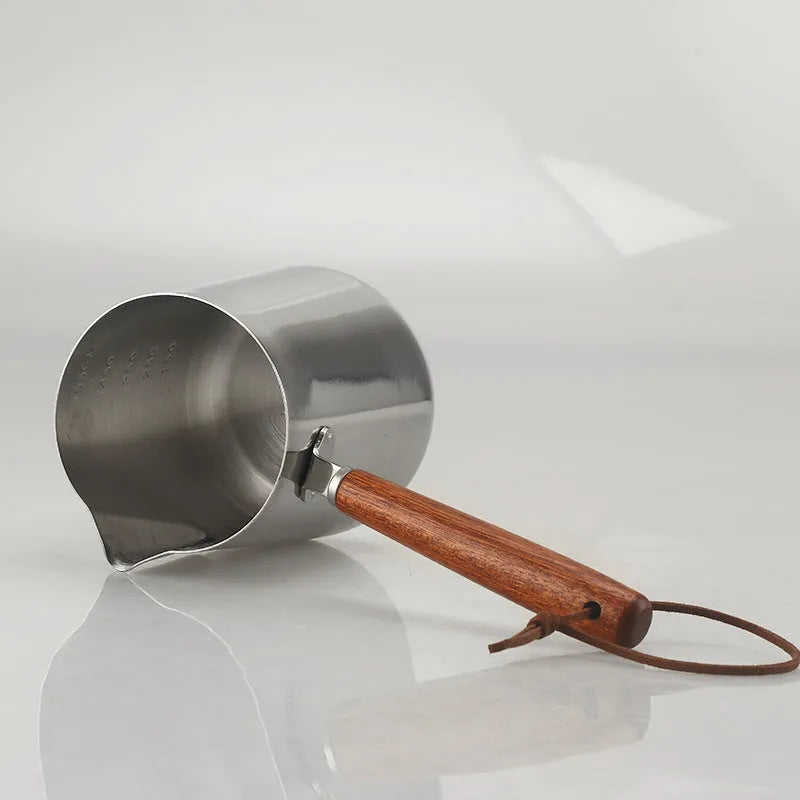Stainless steel latte art milk frothing jug with measurement scale and wooden handle