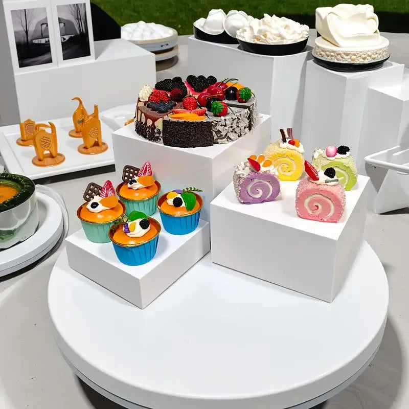 Six white modular plastic cube units arranged as a tiered dessert display stand holding cupcakes.