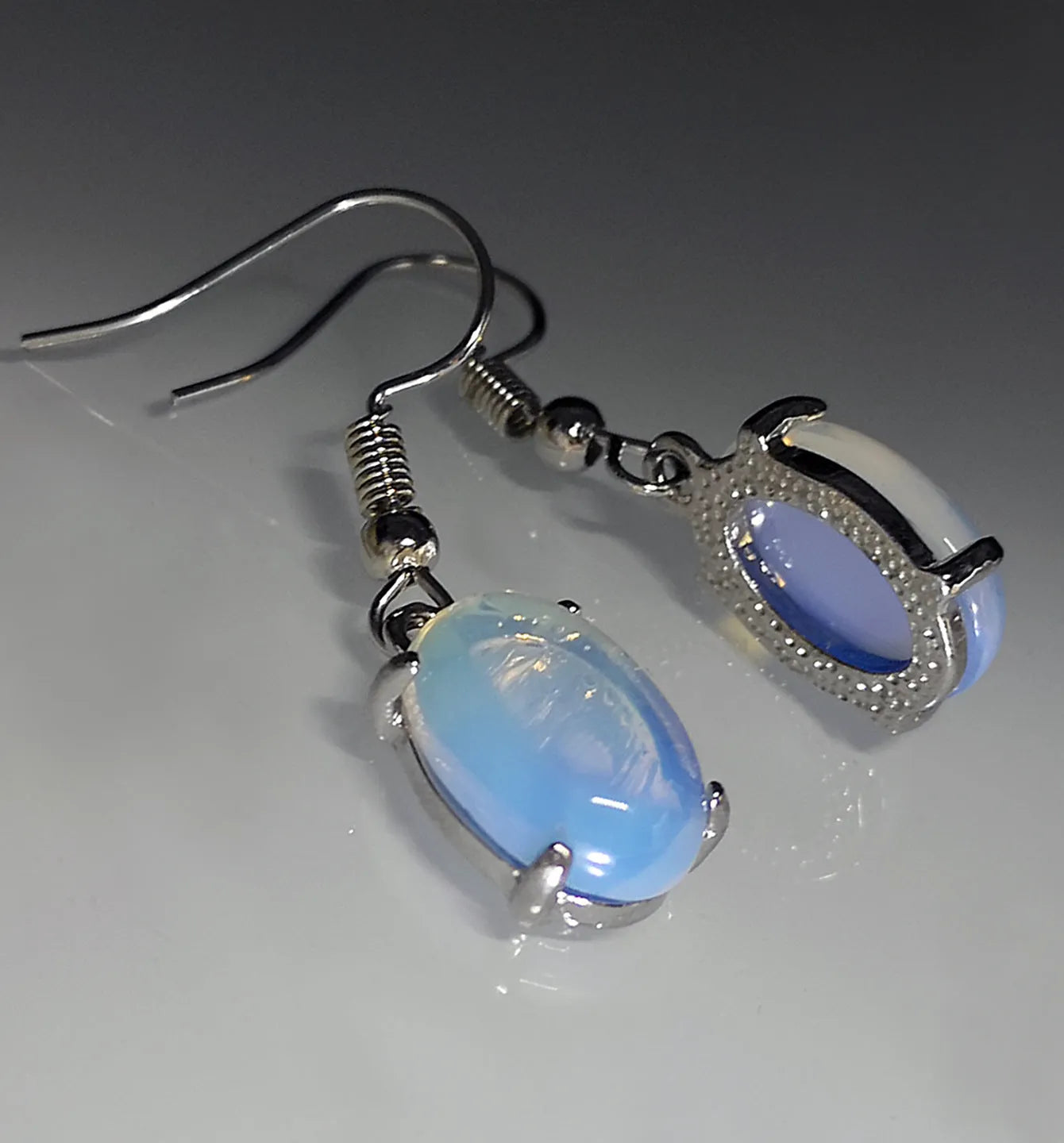A pair of opal-coloured dangle earrings with a cross pendant, in a drop shape on a white background.