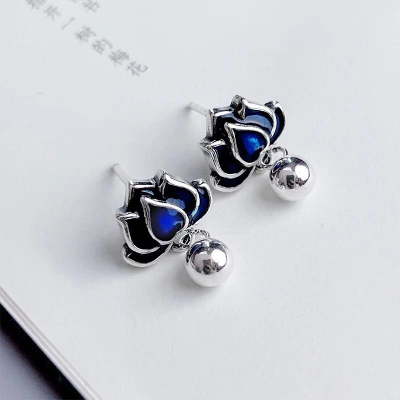 Close-up of blue lotus flower stud earrings with a silver tassel drop on an alloy ear post.