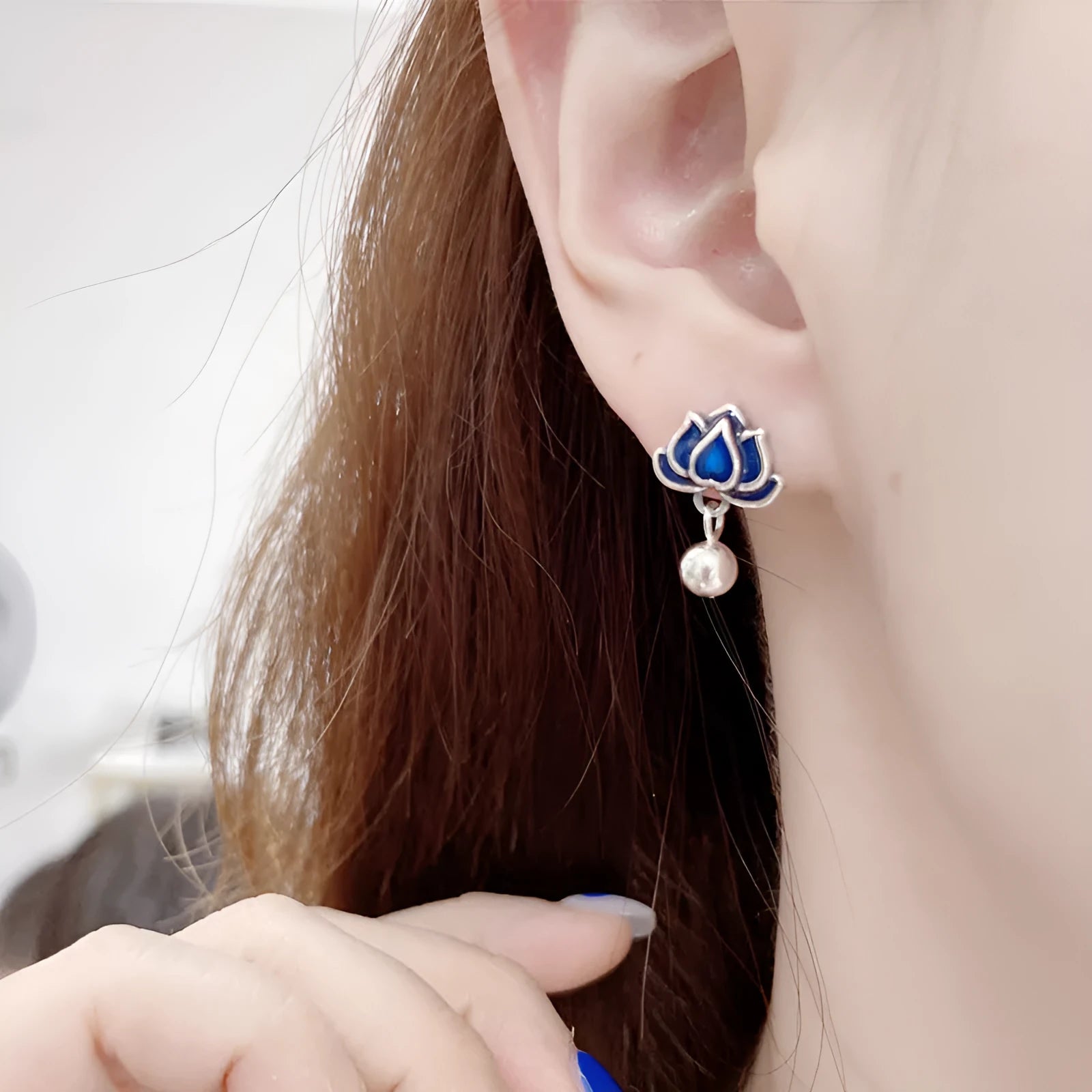 Close-up of blue lotus flower stud earrings with a silver tassel drop on an alloy ear post.