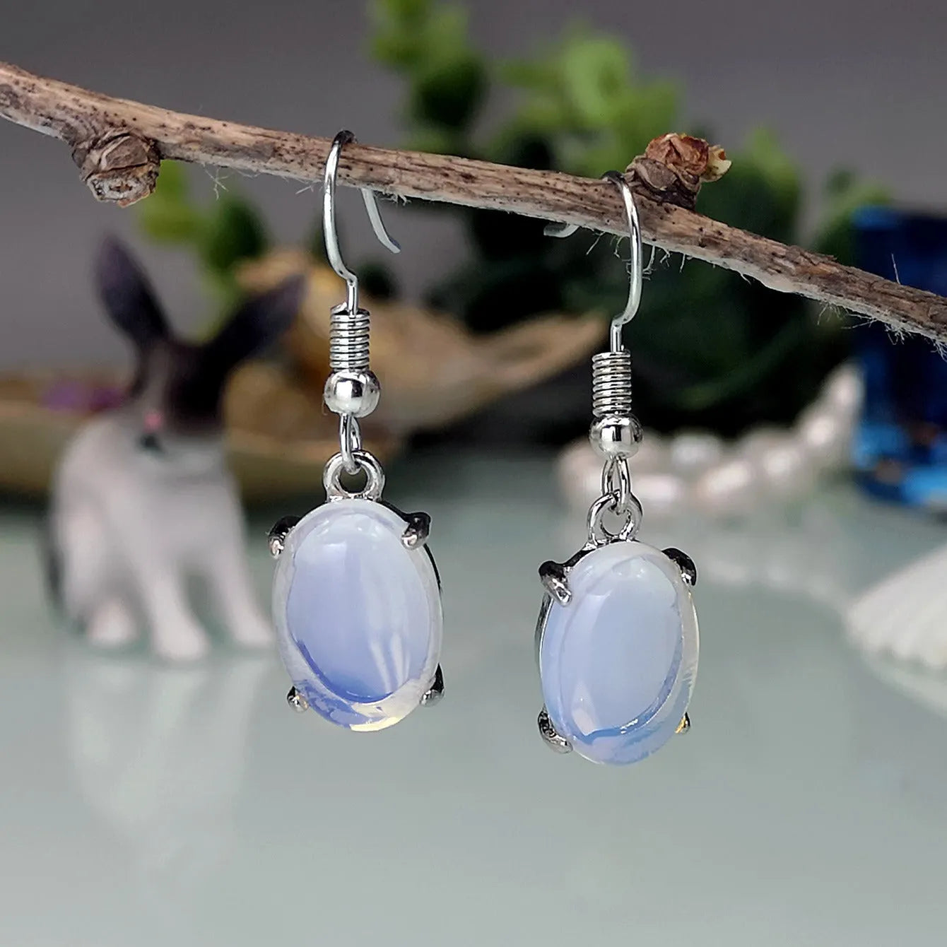 A pair of opal-coloured dangle earrings with a cross pendant, in a drop shape on a white background.
