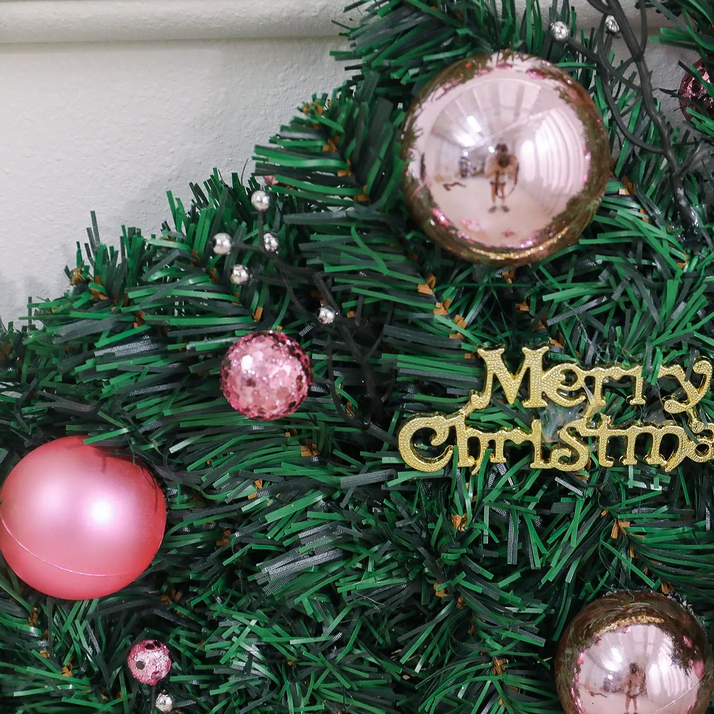 Pink artificial Christmas rattan vine decoration with small fruit clusters and warm white LED lights, coiled on a table.