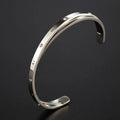Open-ended stainless steel bracelet with a love symbol and zircon stones in gold tone.