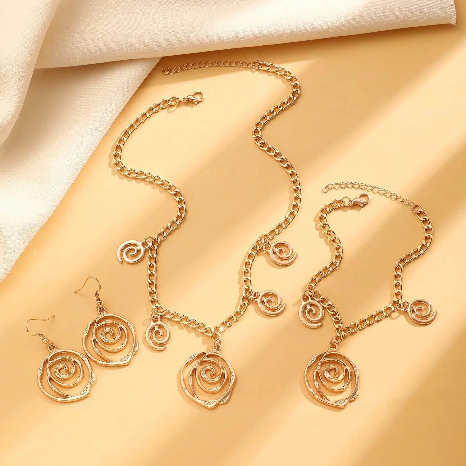 Gold spiral donut charm jewellery set showing necklace, bracelet and earrings on a white background