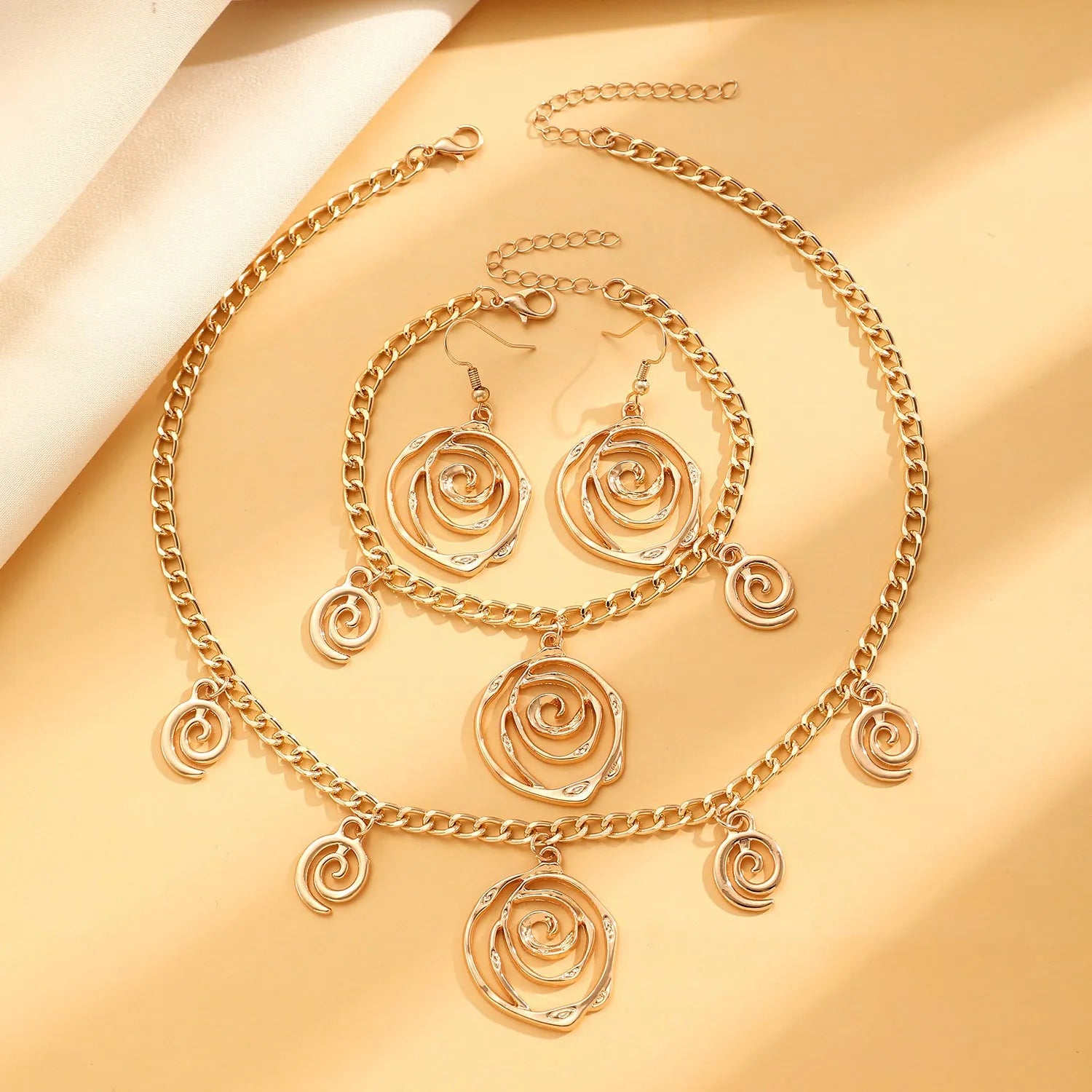 Gold spiral donut charm jewellery set showing necklace, bracelet and earrings on a white background