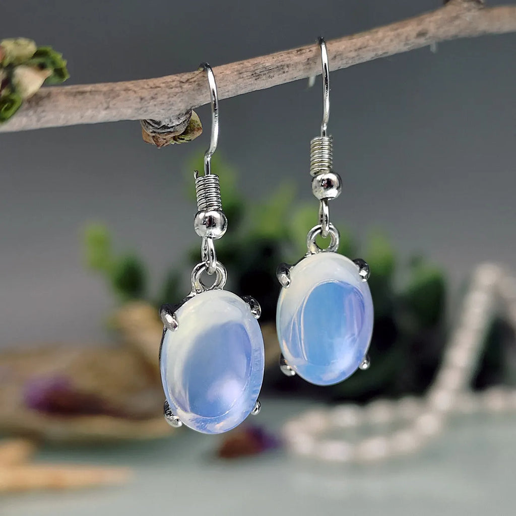 A pair of opal-coloured dangle earrings with a cross pendant, in a drop shape on a white background.