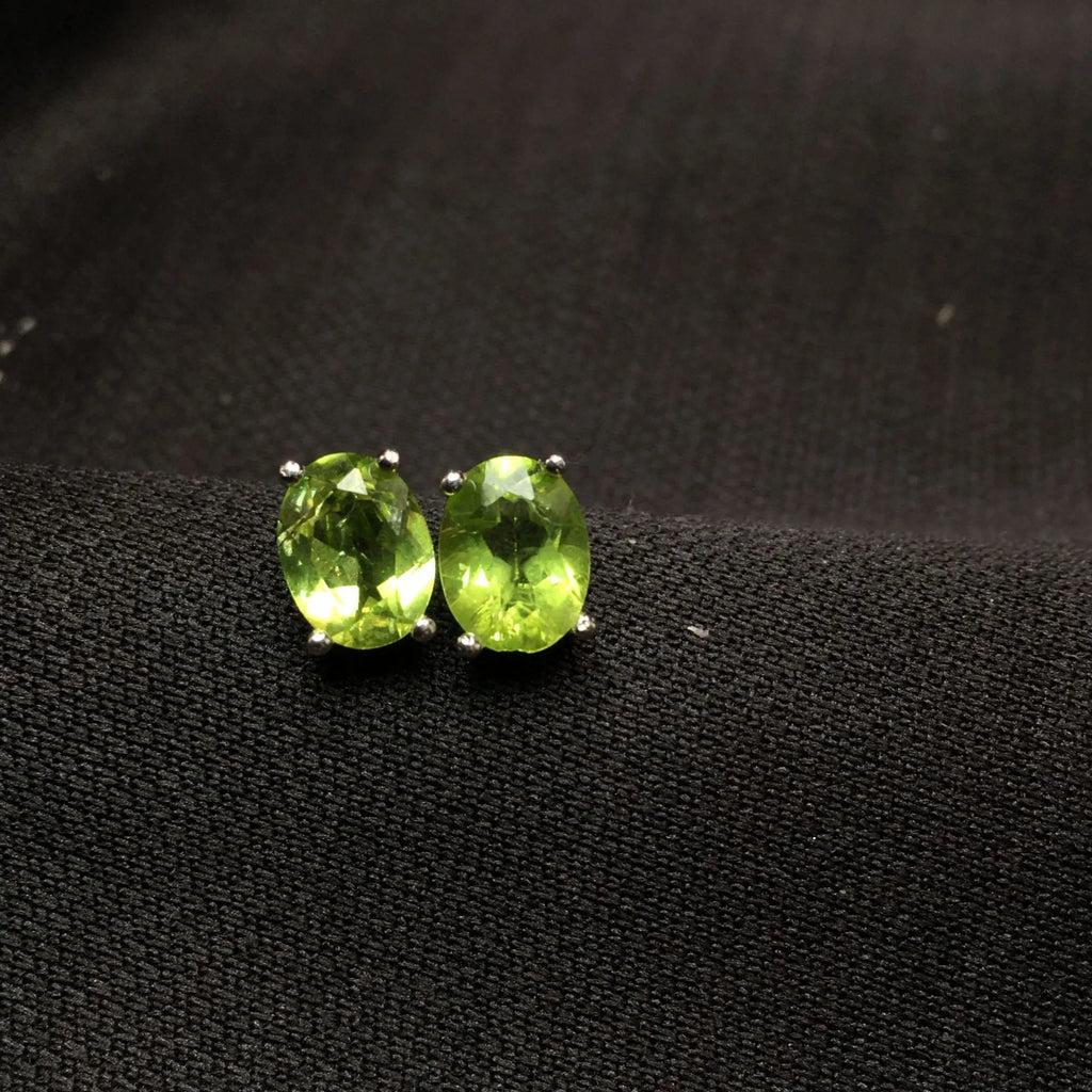 Close-up of grass green olivine stud earrings in sterling silver, showing elliptical faceted stone.