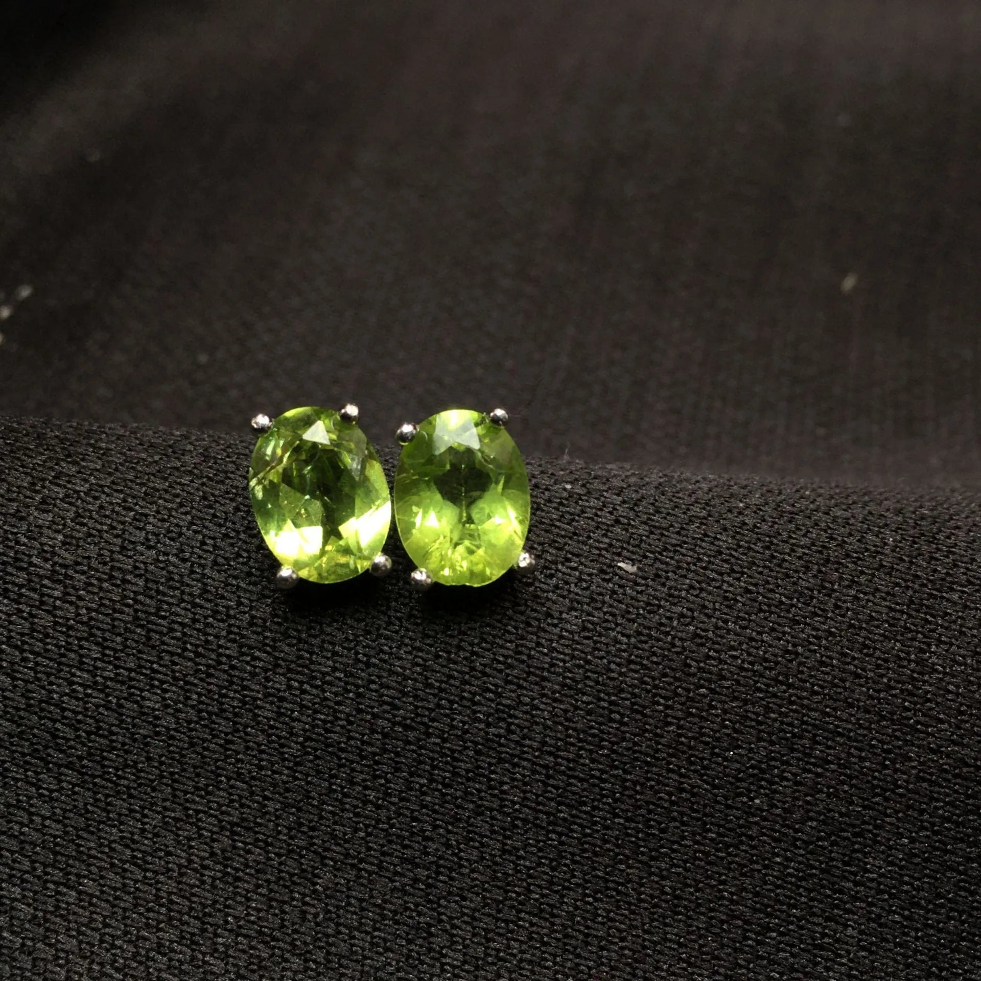 Close-up of grass green olivine stud earrings in sterling silver, showing elliptical faceted stone.
