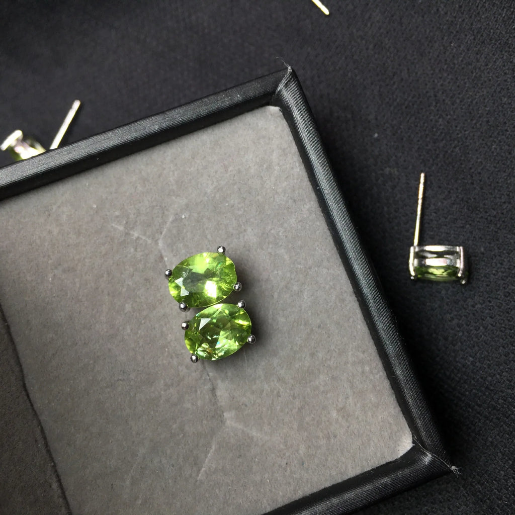 Close-up of grass green olivine stud earrings in sterling silver, showing elliptical faceted stone.