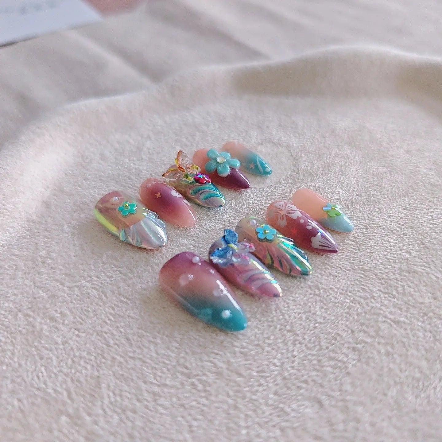 Handmade colourful flower and butterfly sculpture nail art stickers on almond-shaped false nails.