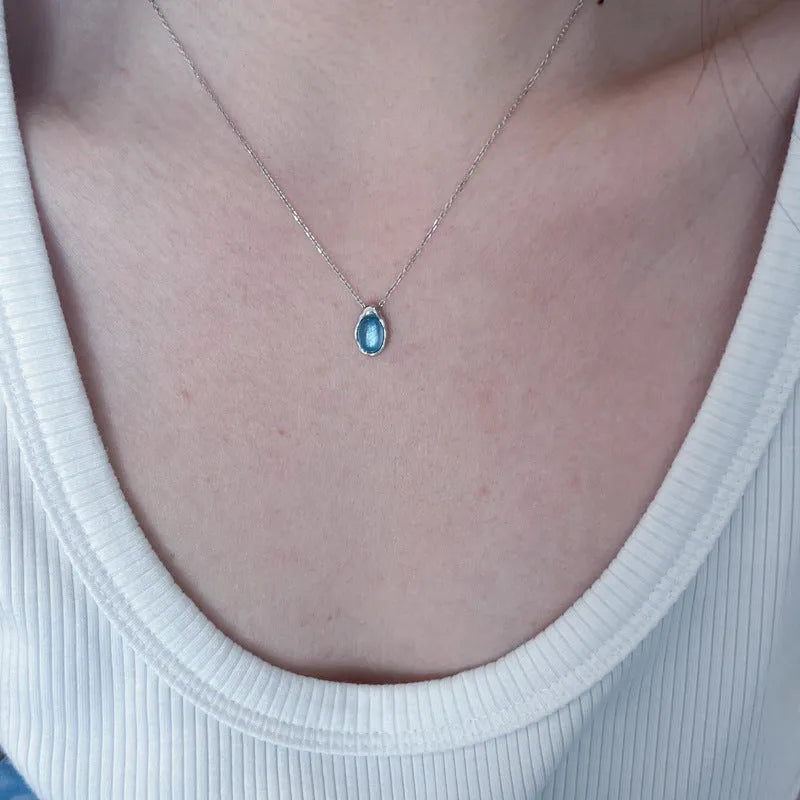 Close-up of a navy blue geometric water drop pendant on a platinum-colour adjustable cross chain necklace.