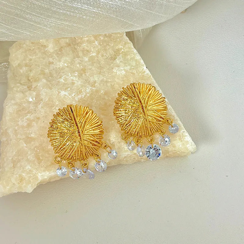 A pair of geometric gold metal earrings with round details on a white background.