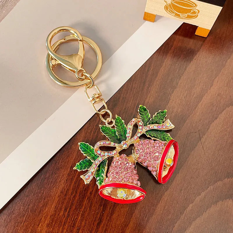 Diamond studded Christmas bell shaped keychain in metal, white diamond colour, on a festive background
