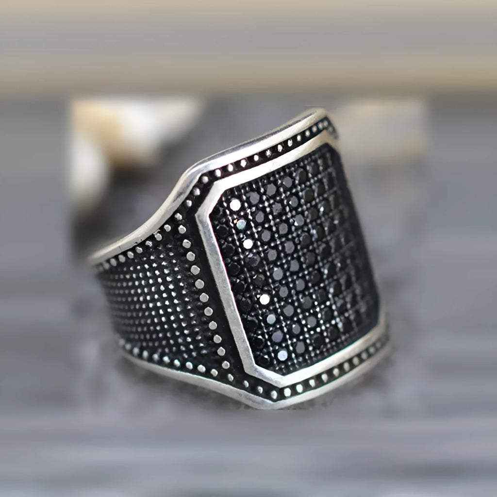 Black alloy ring with copper detailing and a zircon stone, shown in a unisex style.