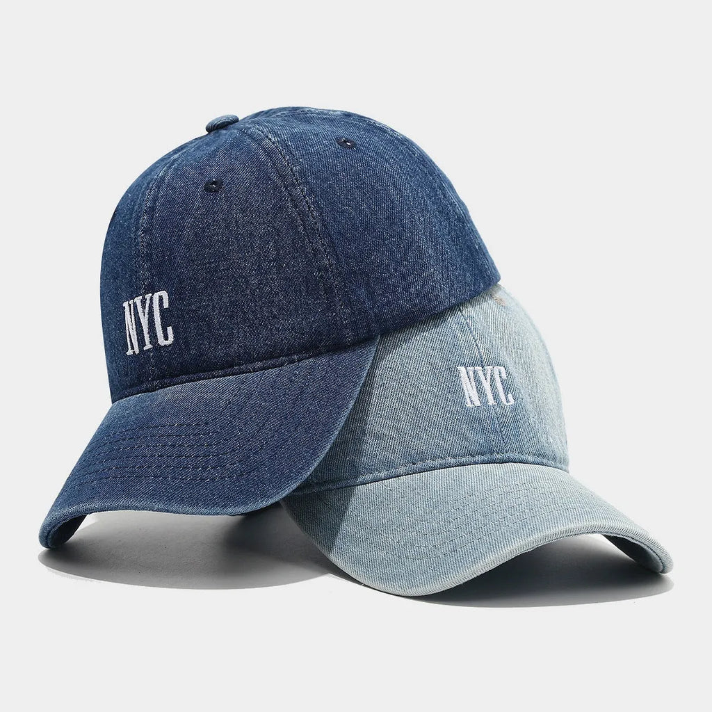 A light blue denim peaked cap with a dome crown, adjustable strap, and decorative white English letters on the front.