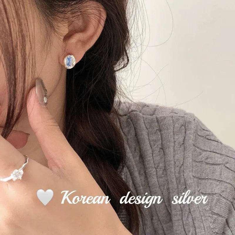 Women's sterling silver oval earrings with heart-wrapped design and blue diamond accents on silver background