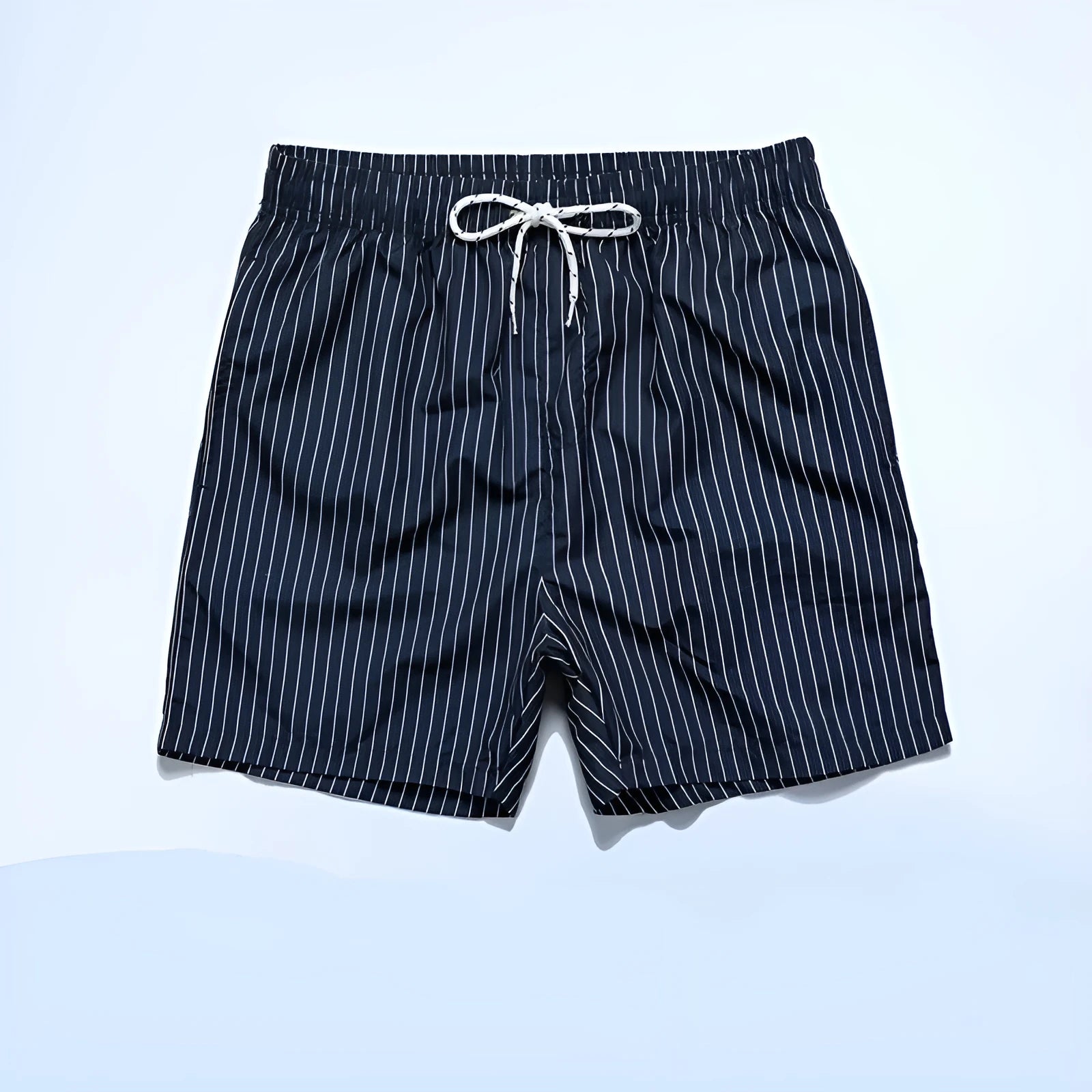 Man wearing navy blue and white striped straight-leg polyester beach shorts on shore.