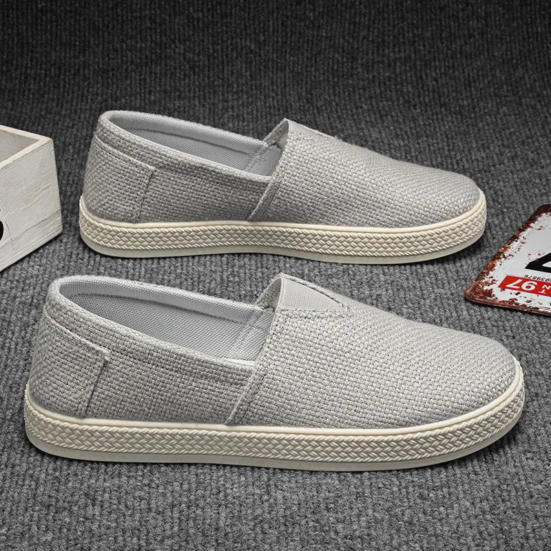 Men's beige canvas slip-on loafers with a round toe and shallow cut on a plain background.