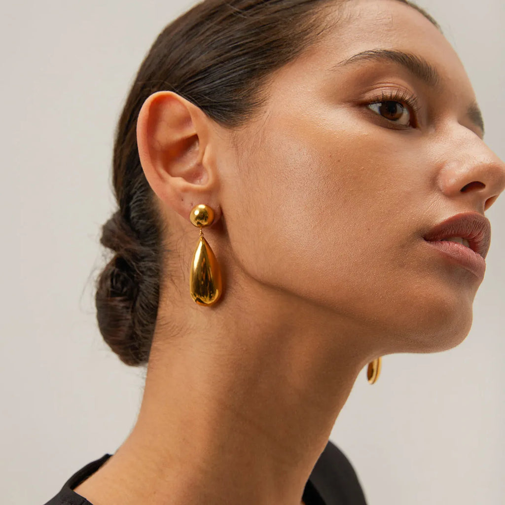 Gold coloured geometric hemisphere earrings with a dangling water drop pendant, made from stainless steel.