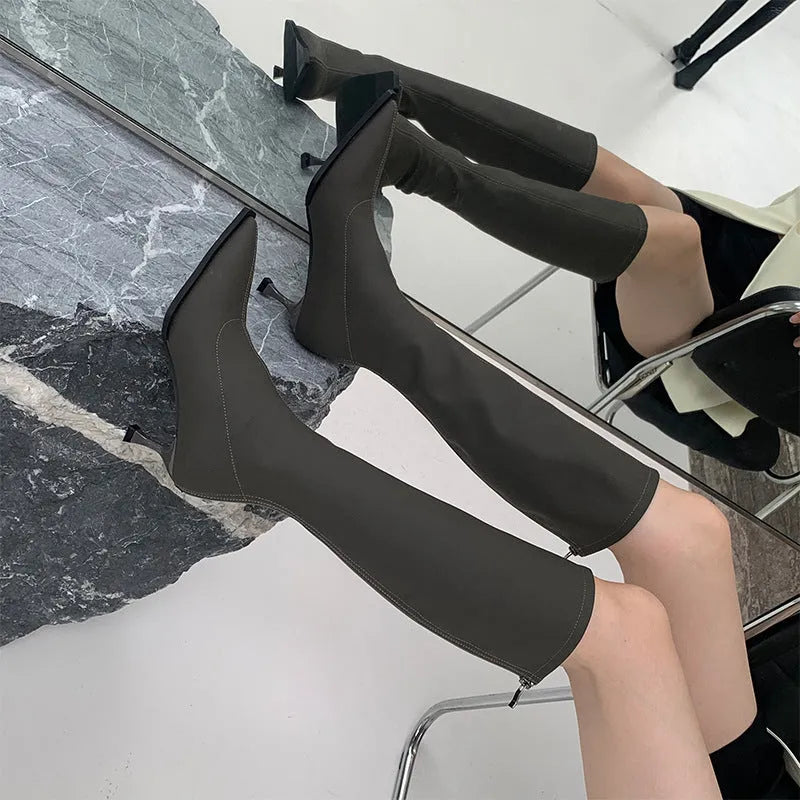 Women's black pointed toe stiletto heel boots with a back zipper, showing the below-the-knee shaft.
