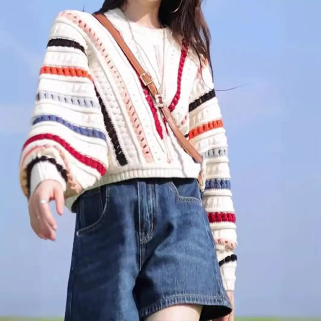 A woman's rainbow striped loose knit sweater with batwing sleeves on a hanger.