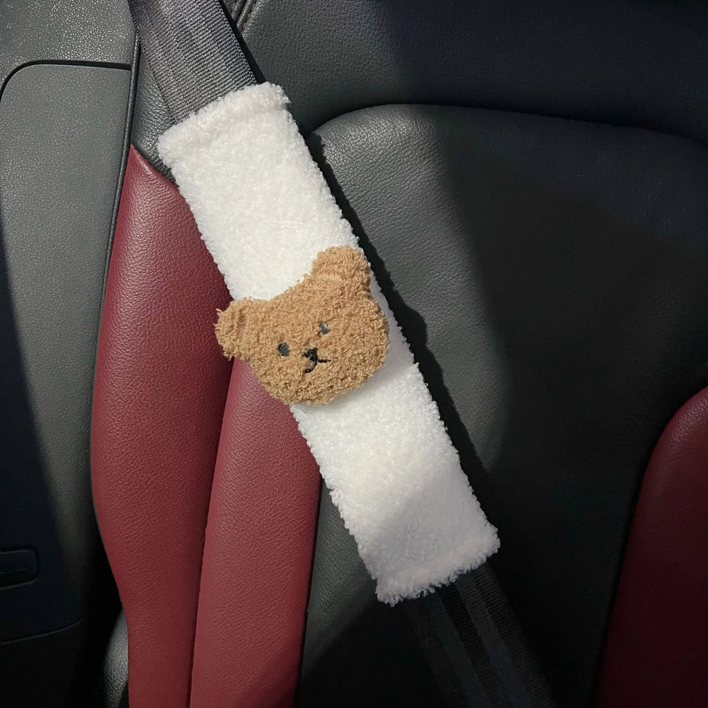 Close-up of a khaki-coloured plush bear seat belt cover on a car seat strap.