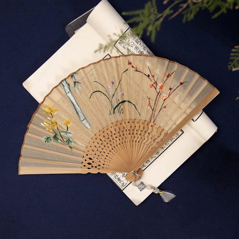 Open bamboo folding fan with detailed Chinese silk embroidery of a butterfly pattern.