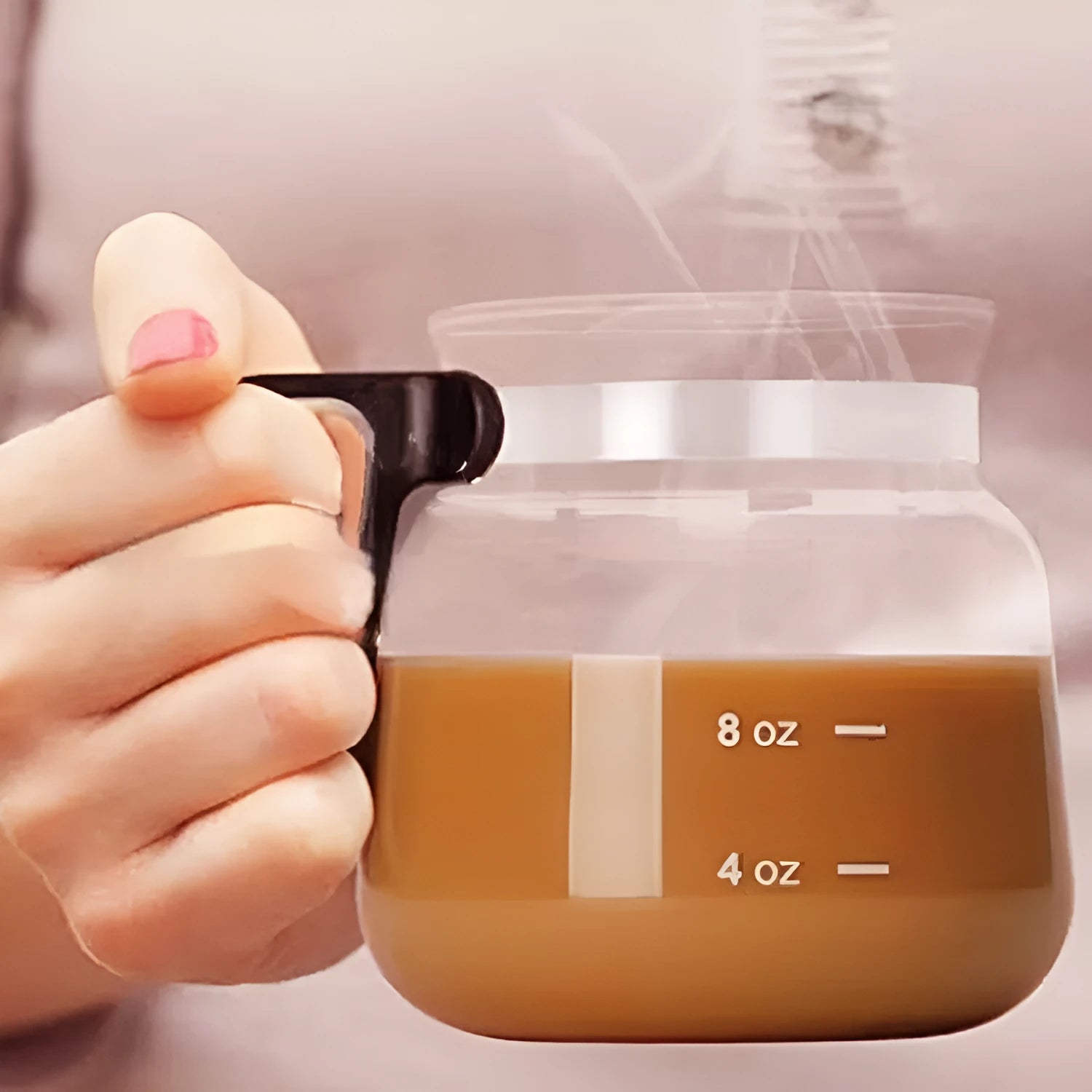 Transparent borosilicate glass stovetop coffee maker with black silicone cover on a hob.
