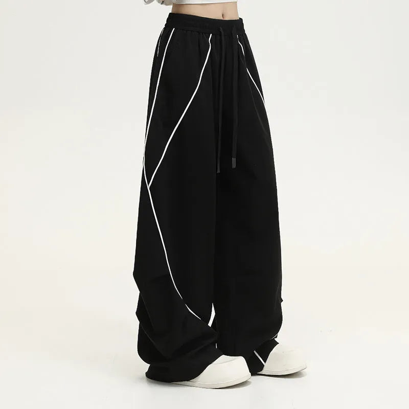 Black trousers with vertical stripes and pleated detail on the legs, showing a loose wide-leg fit.