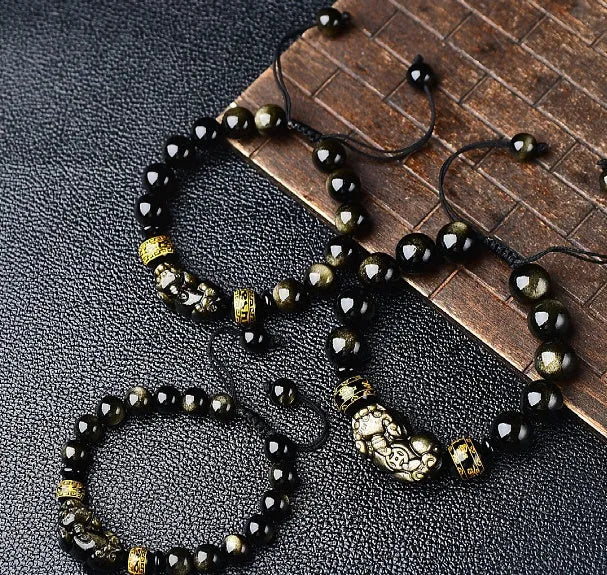 Close-up of a black obsidian bead bracelet with a detailed silver Pi Xiu charm on a neutral background.
