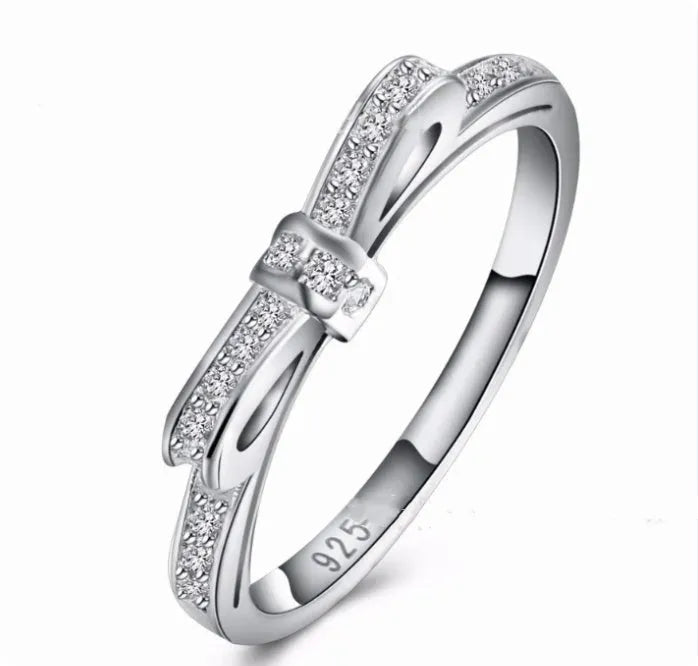 Silver coloured bow-shaped ring with rhinestone and zircon crystal details on a model finger.