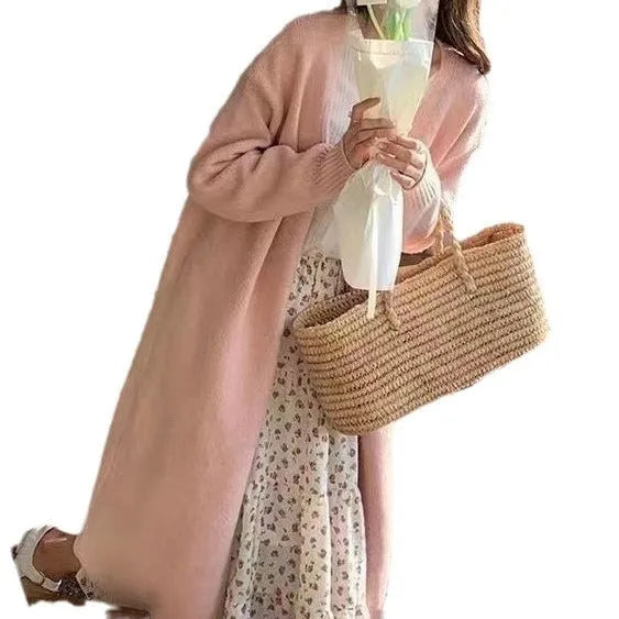 A woman wearing a khaki, mid-length, knitted V-neck cardigan with long sleeves.
