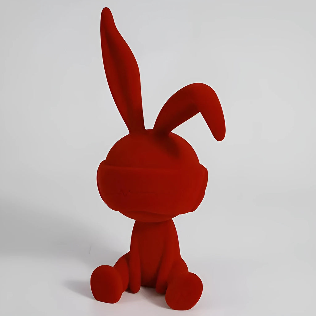 Green resin blindfold rabbit table ornament with suede details on a wooden shelf.