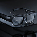 Black smart Bluetooth glasses with a built-in camera lens on the frame, shown with charging cable and case.