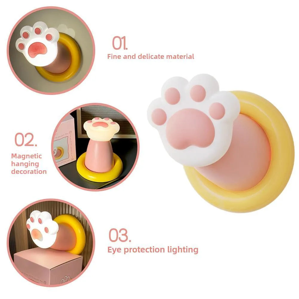 White rechargeable cat paw touch lamp with adhesive back, lit on a bedside table.