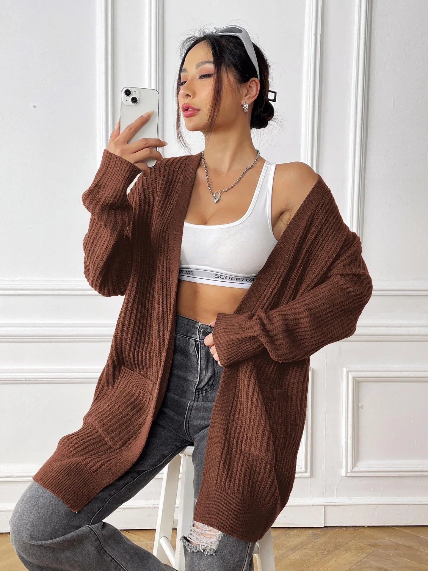 A woman's loose-fit mid-length cardigan in a solid colour, shown on a hanger.
