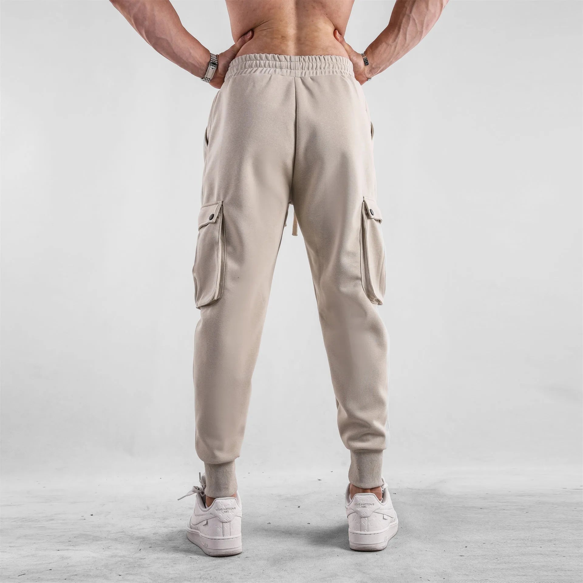 Men's loose beige cotton trousers with an ankle tie and multiple pockets on a casual model.