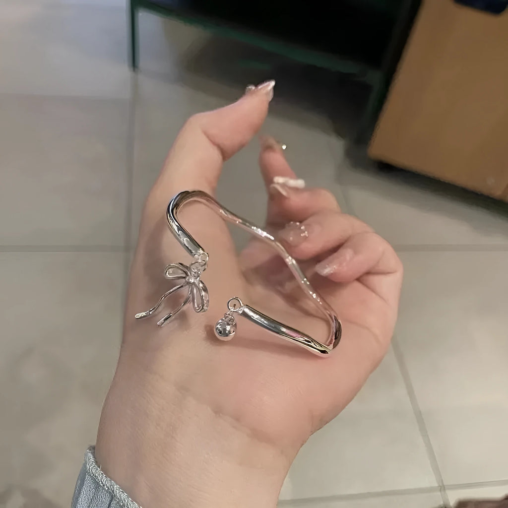 Silver-coloured adjustable bracelet with a bow charm on a wrist.