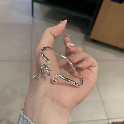 Silver-coloured adjustable bracelet with a bow charm on a wrist.