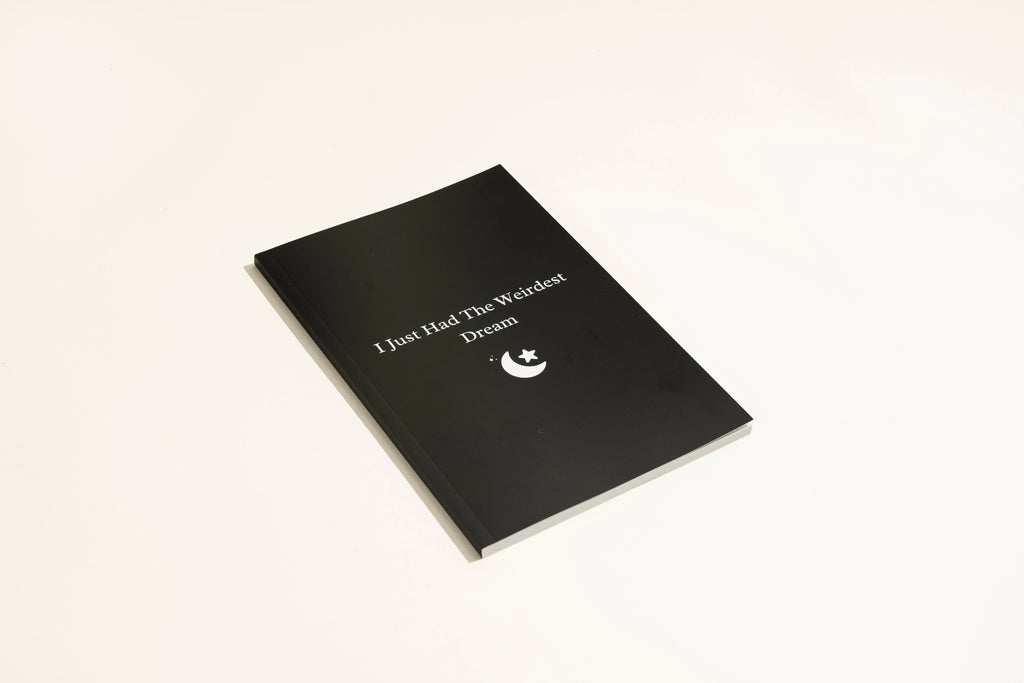 Black hardcover dream journal notebook with plain paper pages open on a desk.