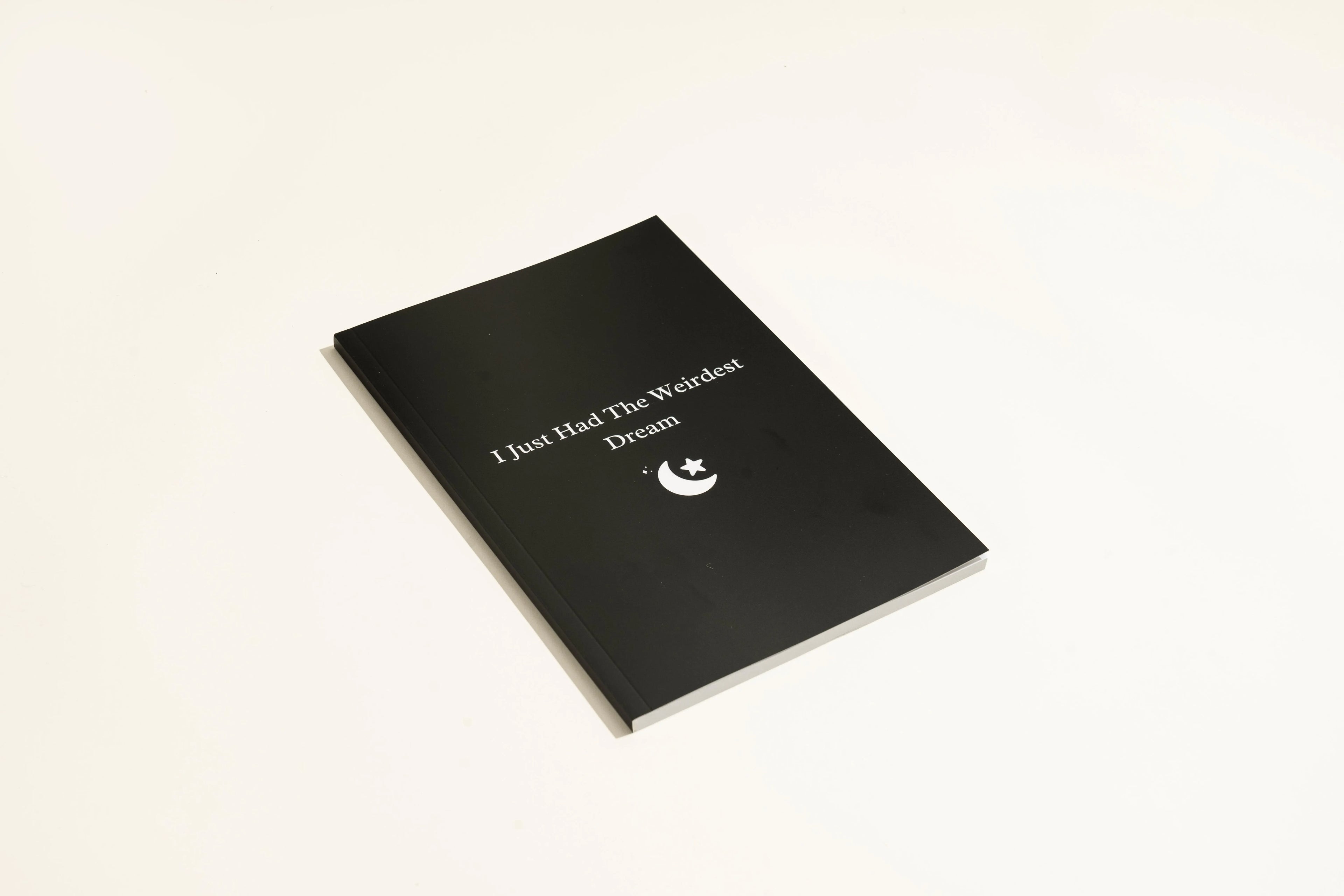 Black hardcover dream journal notebook with plain paper pages open on a desk.