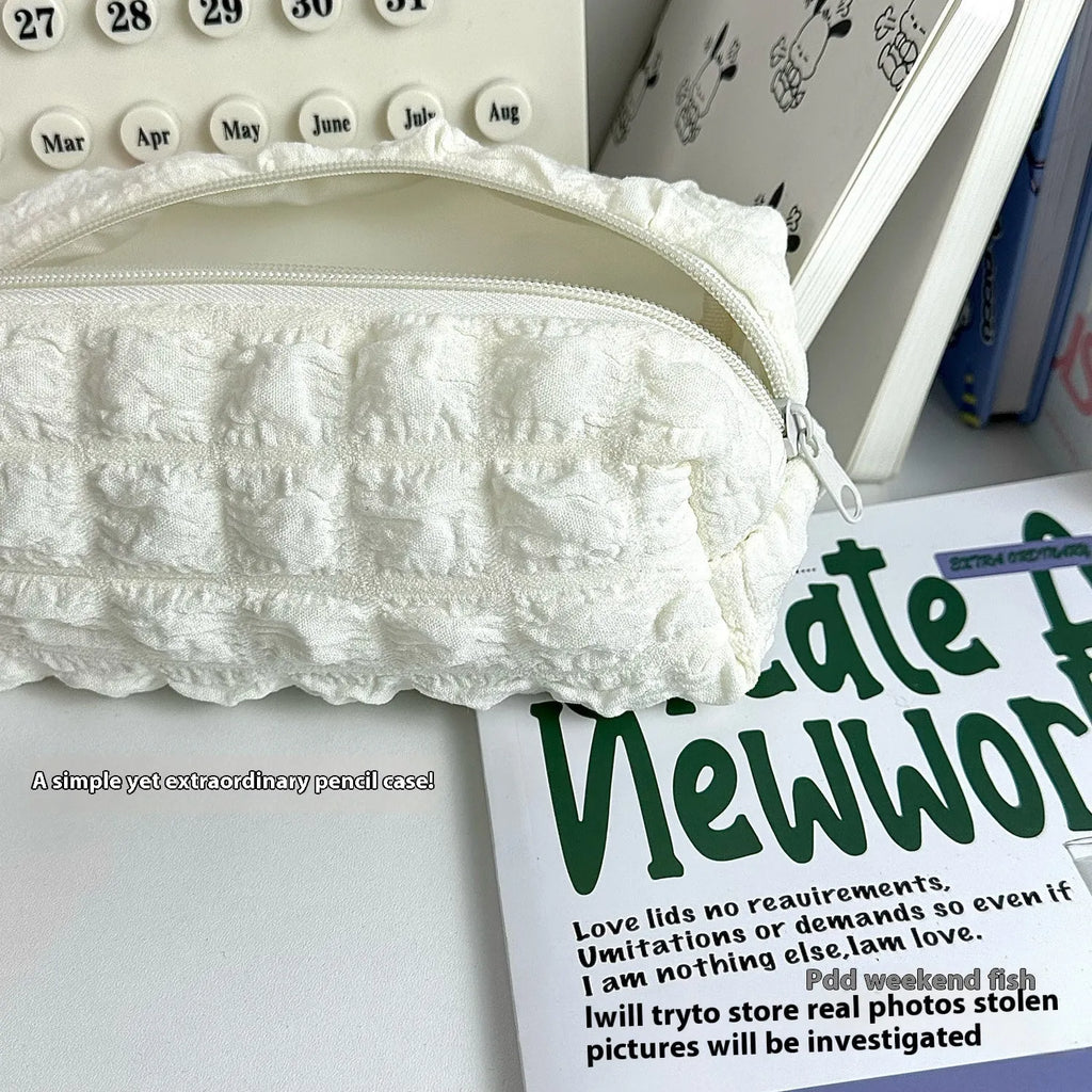 Beige fabric pencil case with cream puff design and zip closure next to pens.