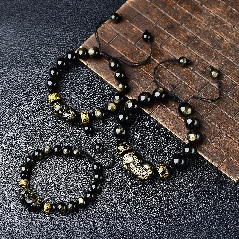 Close-up of a black obsidian bead bracelet with a detailed silver Pi Xiu charm on a neutral background.