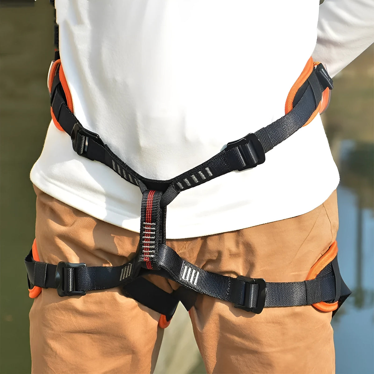 Orange half seat belt climbing safety belt with adjustable waist and leg straps on outdoor rock background