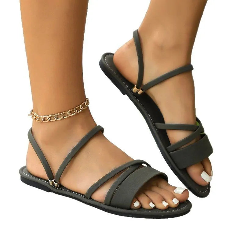 Women's flat black sandals with flip-toe design, ankle buckle, and cross-strap.