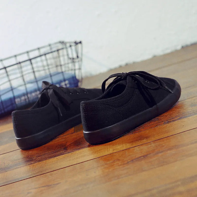 All black canvas low-top lace-up flat shoes for women on a white background